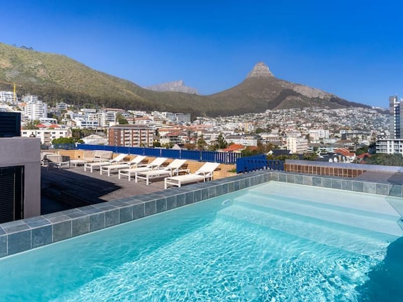 Rooftop swimming pool with timber decking and metal balustrades, offering panoramic mountain and city views.