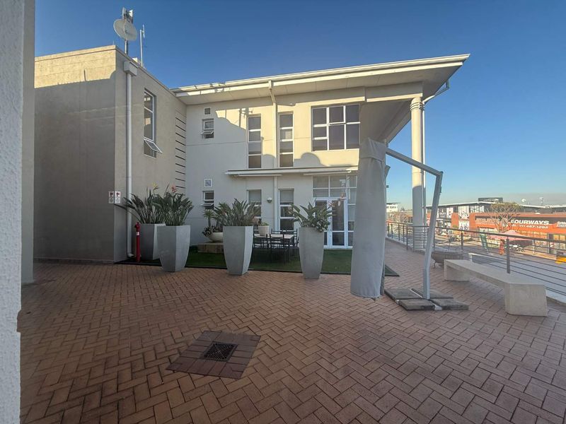 Spacious paved outdoor terrace area featuring a modern building facade, integrated drainage, and perimeter railings, suitable for office break-out space.