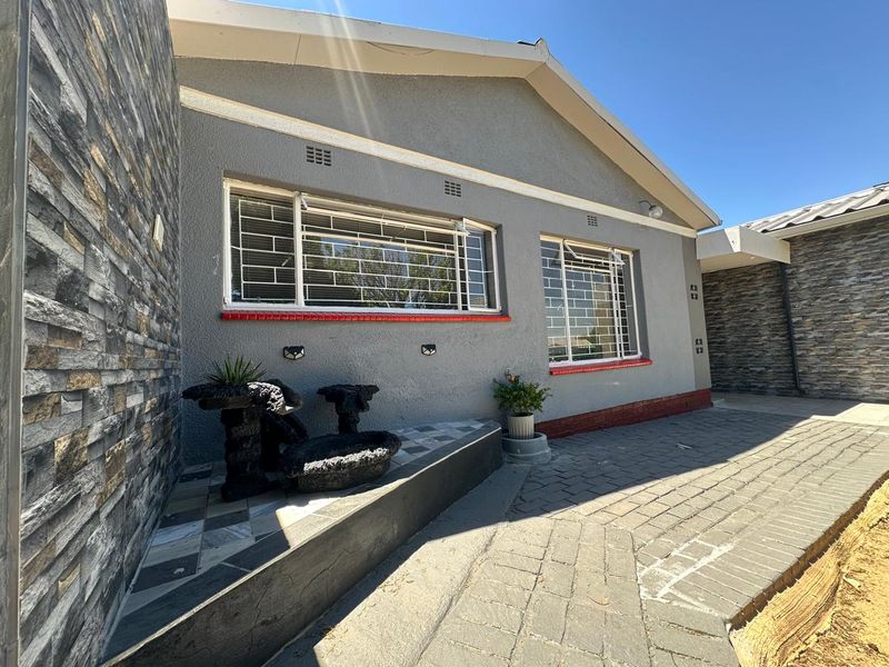 A well-maintained rear exterior area featuring stone-clad walls, paved patio flooring, and secure windows with fitted security bars.