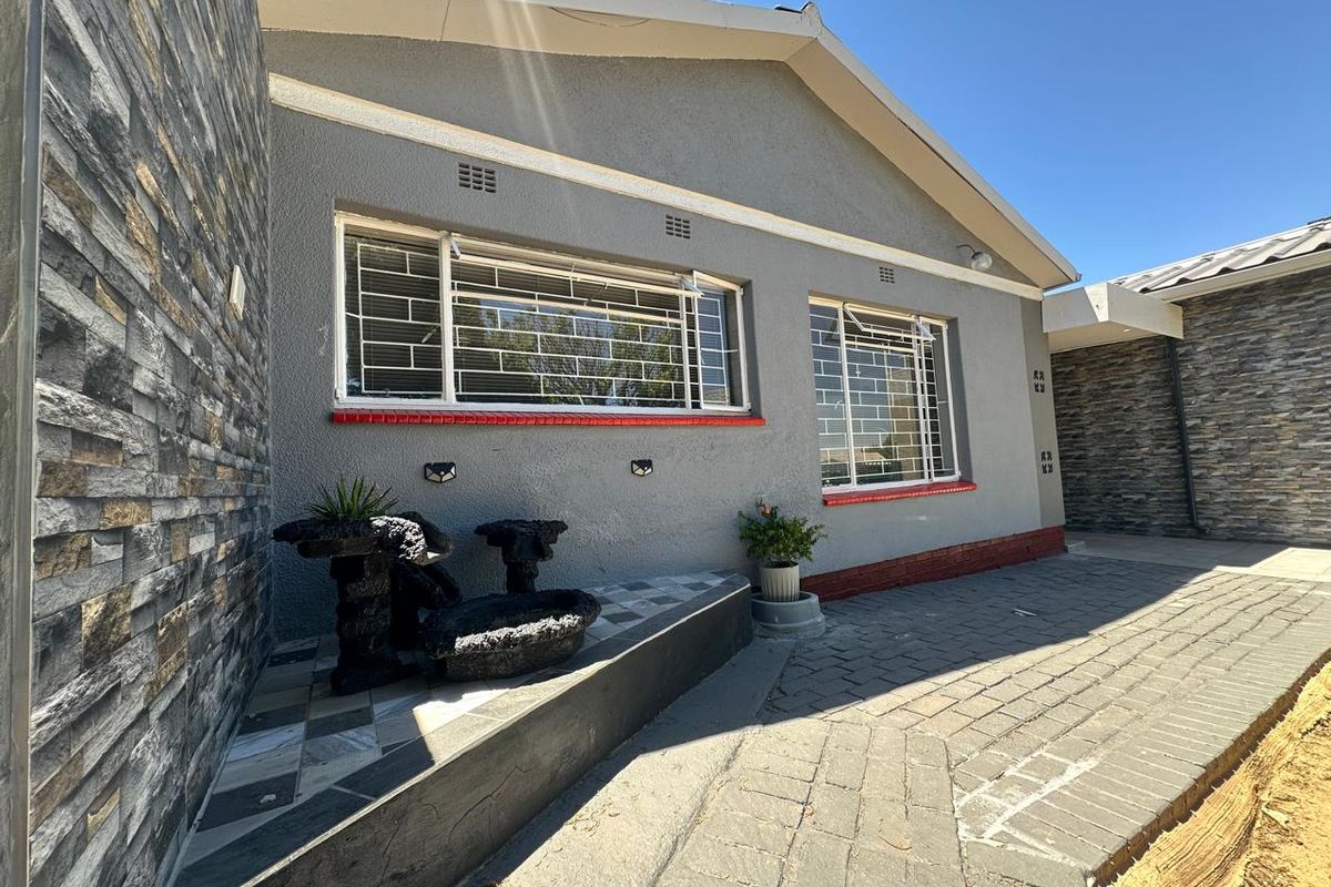 A well-maintained rear exterior area featuring stone-clad walls, paved patio flooring, and secure windows with fitted security bars.