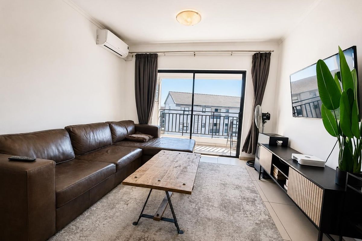 A bright living room featuring tiled flooring, a wall-mounted air conditioning unit, and a sliding glass door providing access to a balcony.