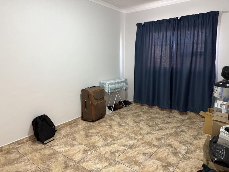 A simple, neutrally painted bedroom featuring tiled flooring and window curtain tracks, offering a blank canvas for potential interior design updates.