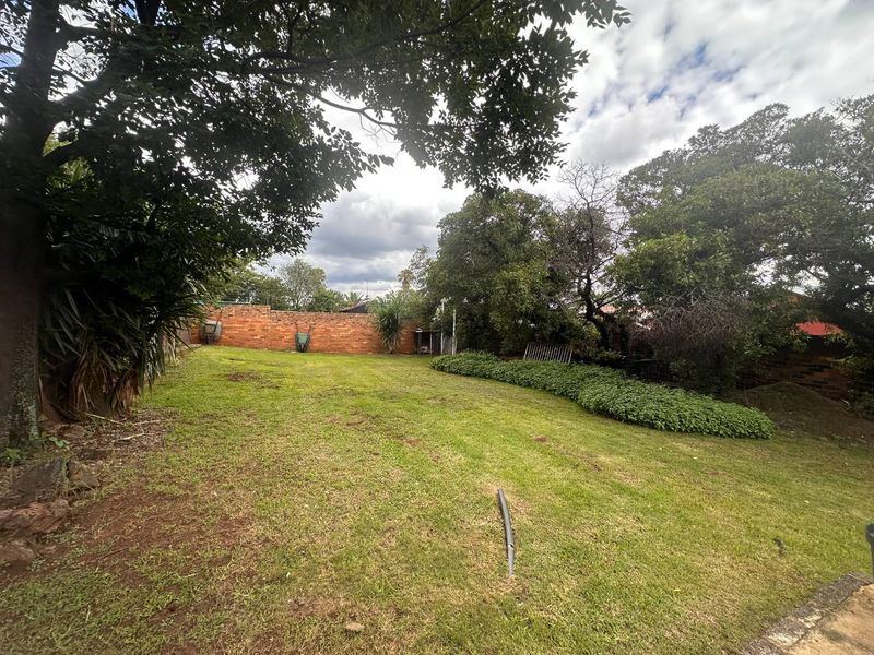 A spacious, established rear garden featuring a large lawn area, mature trees, and a brick boundary wall.