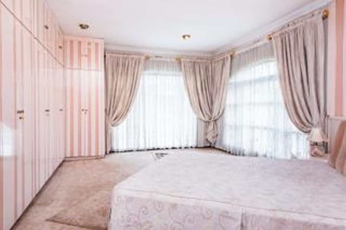 A spacious bedroom featuring extensive built-in floor-to-ceiling cabinetry, large windows with draped curtains, and neutral carpeting.