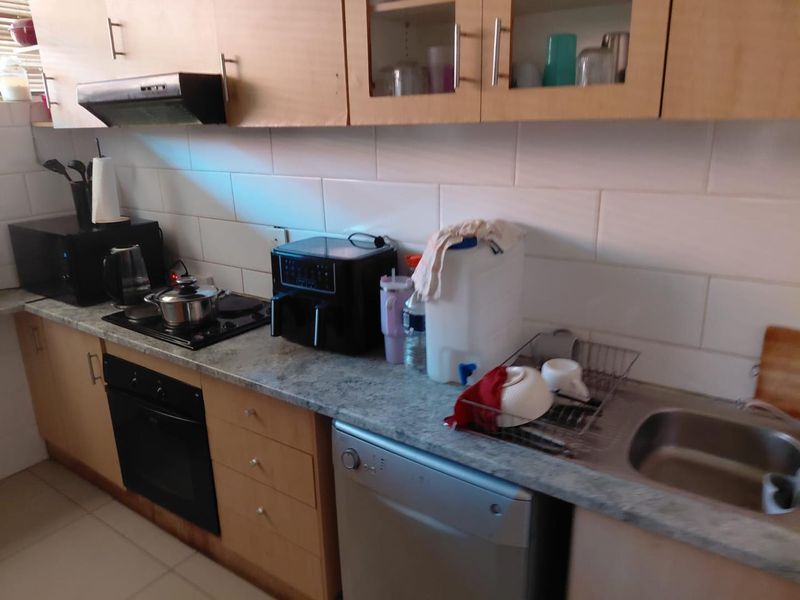 A functional kitchen featuring light wood cabinetry, a tiled backsplash, built-in oven, electric hob, and a stainless steel sink with laminate countertops.