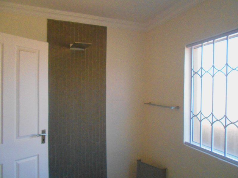 A functional bathroom featuring a tiled shower area, security bars on the window, and a wall-mounted towel rail.