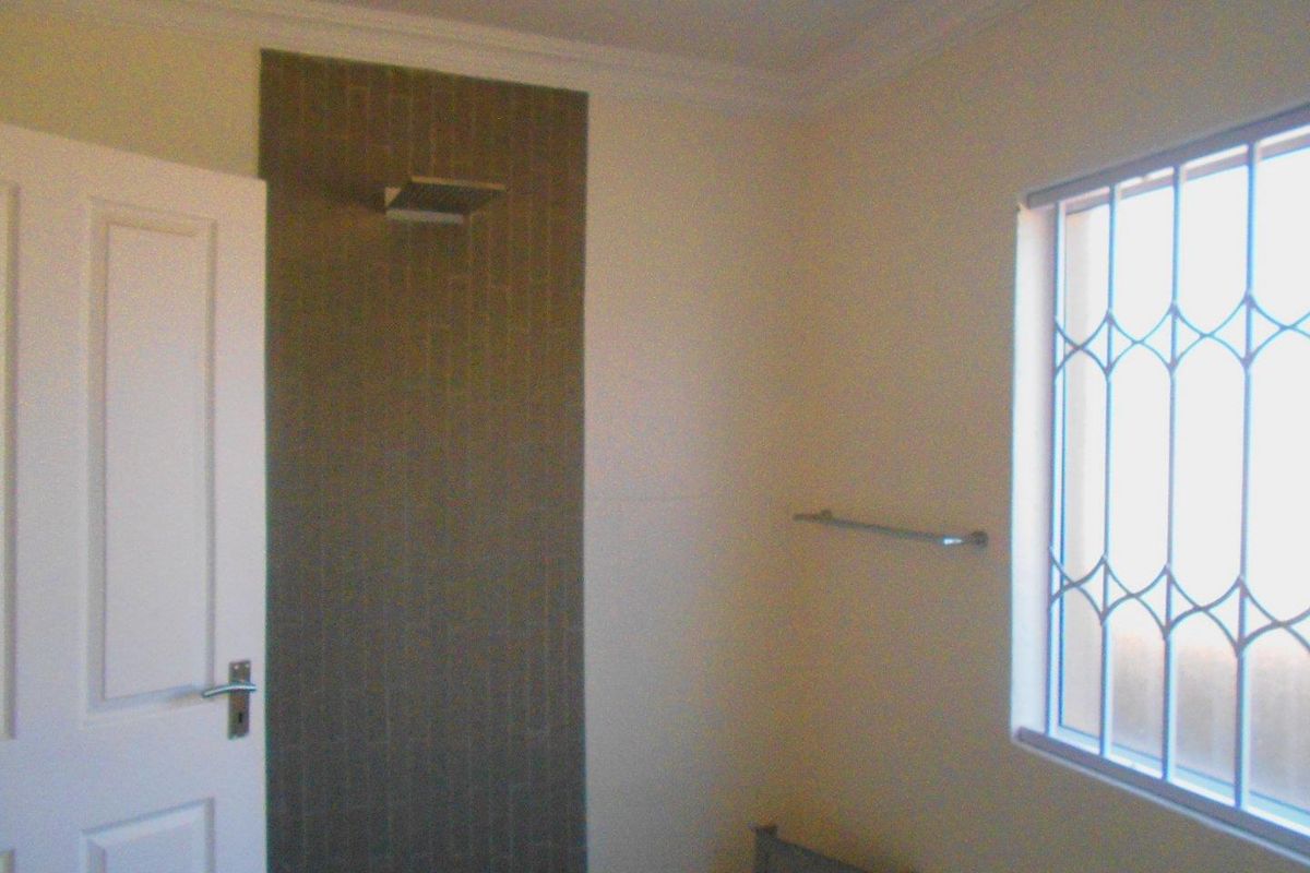 A functional bathroom featuring a tiled shower area, security bars on the window, and a wall-mounted towel rail.