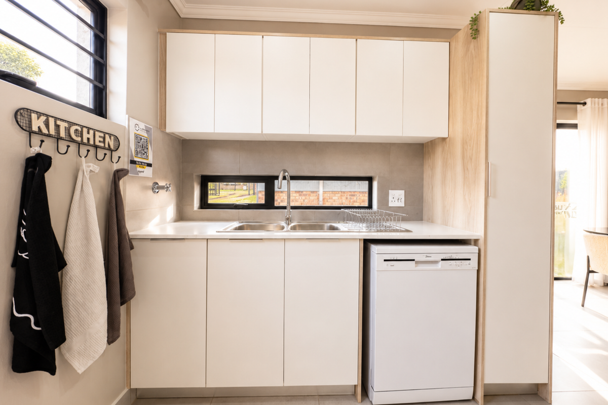 A modern, compact kitchen area featuring sleek white cabinetry, a double stainless steel sink, and a dedicated space for a dishwasher.