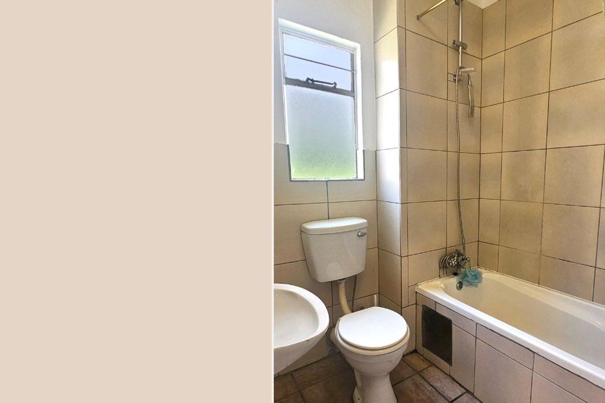 A dated bathroom featuring a standard bathtub with shower attachment, pedestal basin, and toilet, finished with neutral wall tiles and ceramic floor tiles.