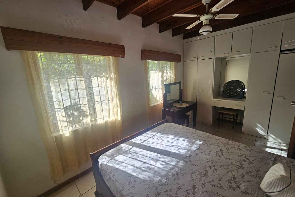 A bedroom featuring exposed timber ceiling beams, built-in cupboards with an integrated vanity, and tiled flooring.