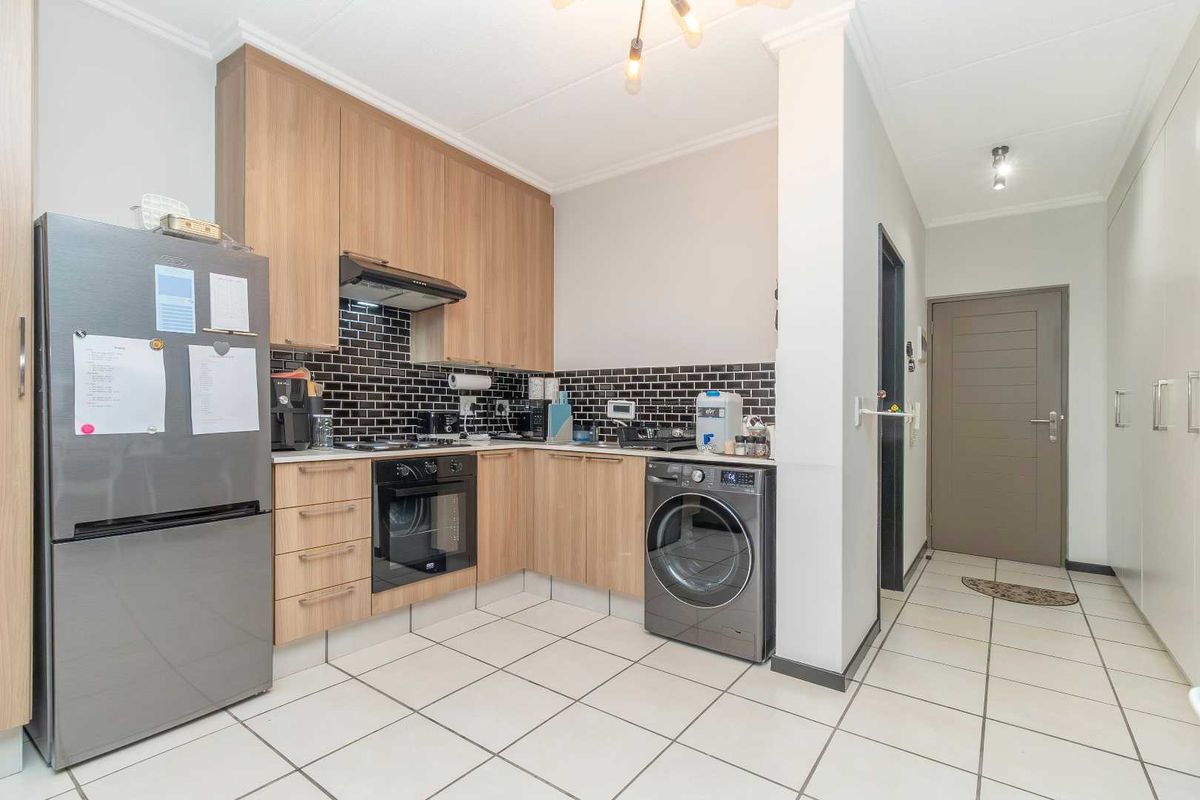 Modern kitchen featuring light wood cabinetry, black subway tile backsplash, built-in oven, extractor fan, and tiled flooring, adjacent to a hallway entrance.