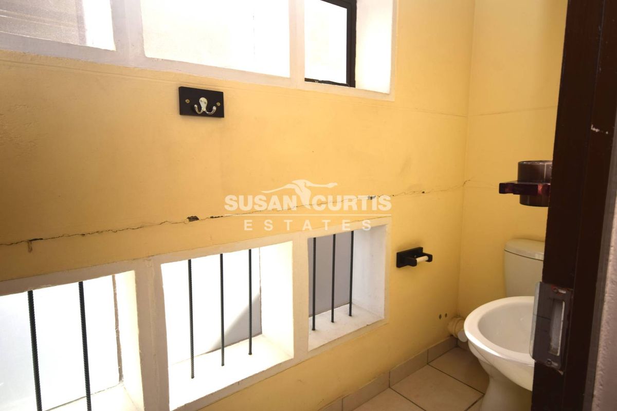 A small industrial-style bathroom featuring tiled flooring, a toilet, and security bars on the windows, requiring cosmetic updates to the wall finishes.