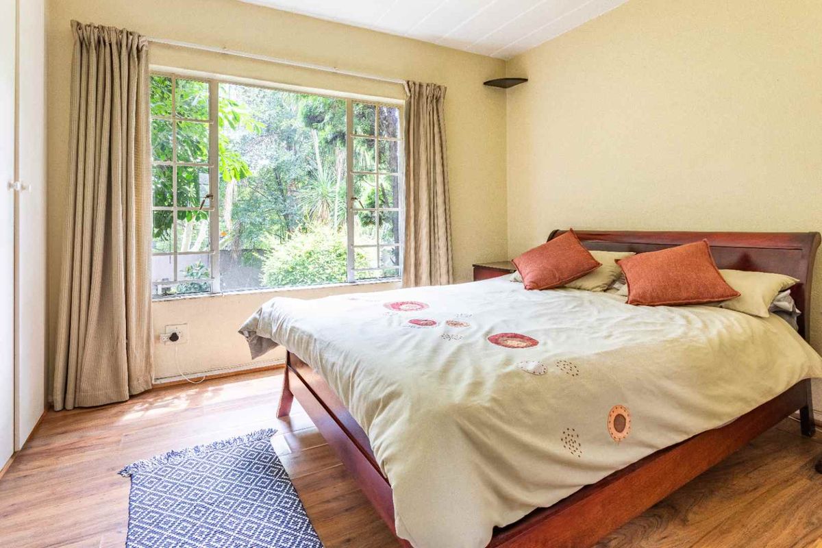 A bedroom featuring wood-look flooring, large windows with garden views, and built-in cupboard space.