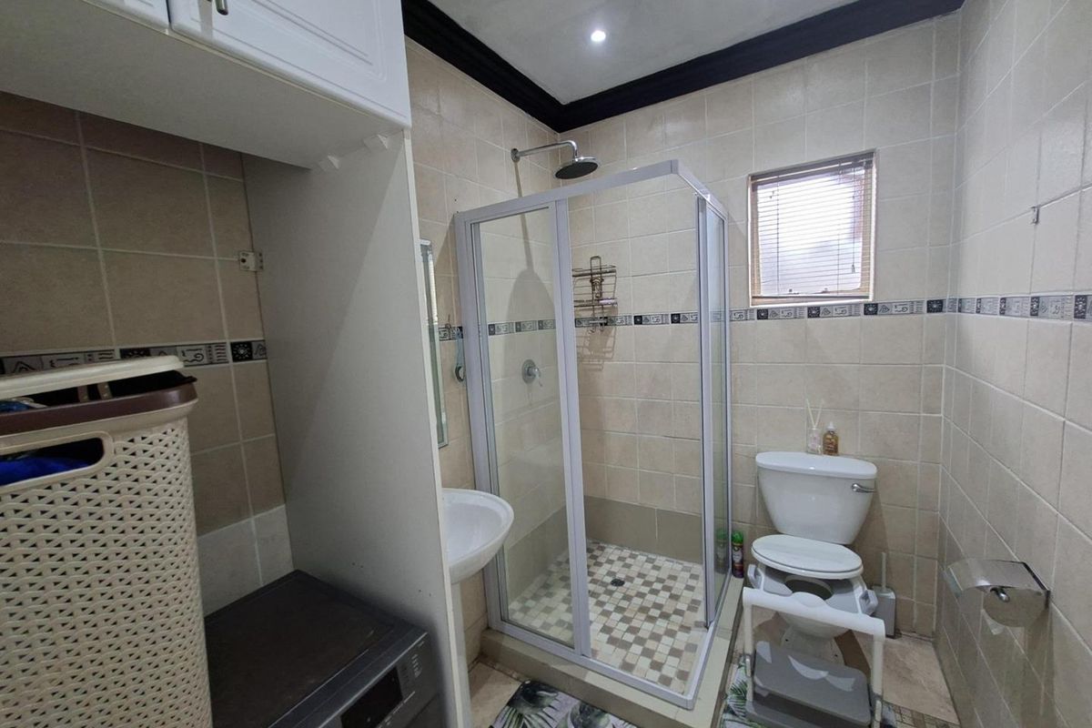 A functional bathroom featuring a glass-enclosed shower, pedestal basin, and toilet, finished with neutral wall tiling and a dark crown molding.