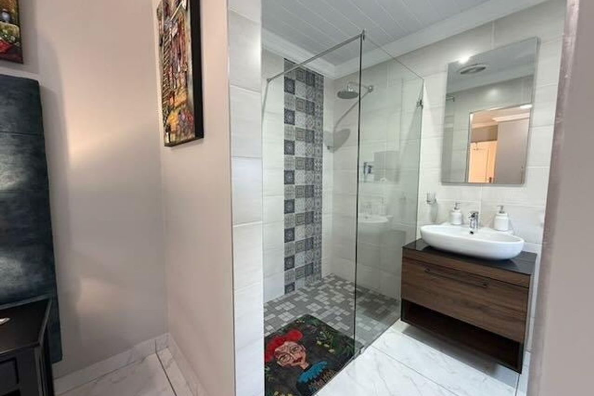 Modern bathroom featuring a glass-enclosed walk-in shower with decorative tile accents, a floating vanity with a vessel sink, and polished floor tiles.