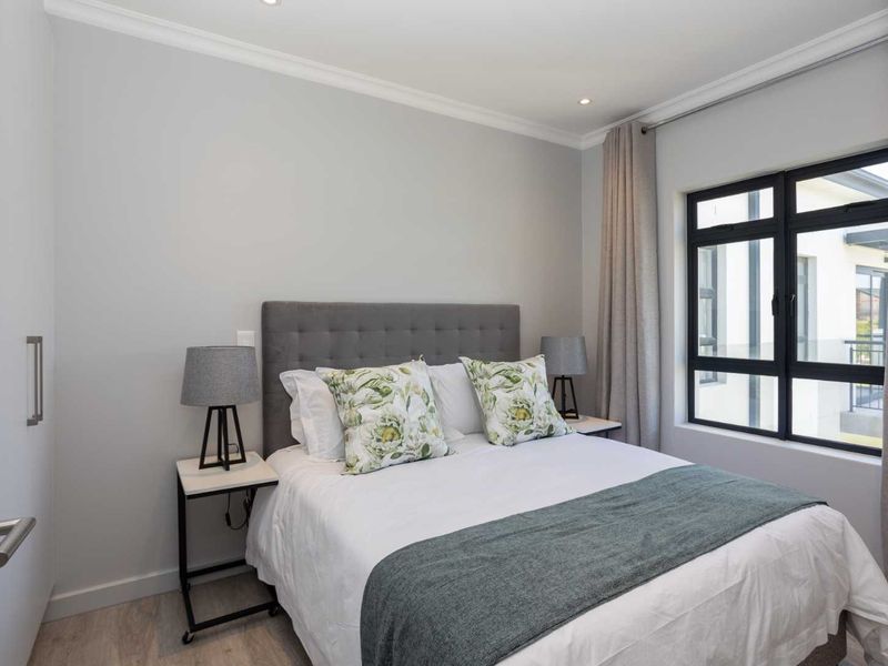 A well-maintained bedroom featuring neutral walls, recessed lighting, and a large black-framed window that allows for natural light.