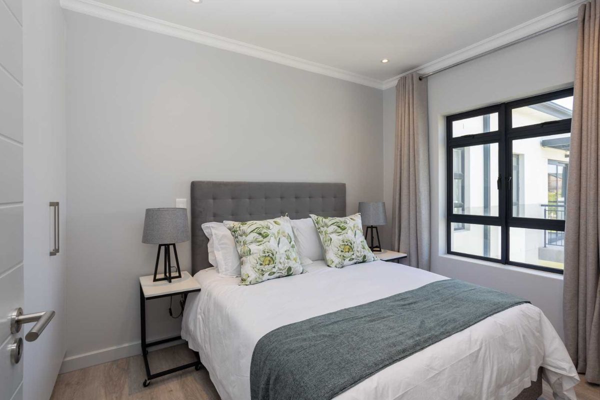 A well-maintained bedroom featuring neutral walls, recessed lighting, and a large black-framed window that allows for natural light.