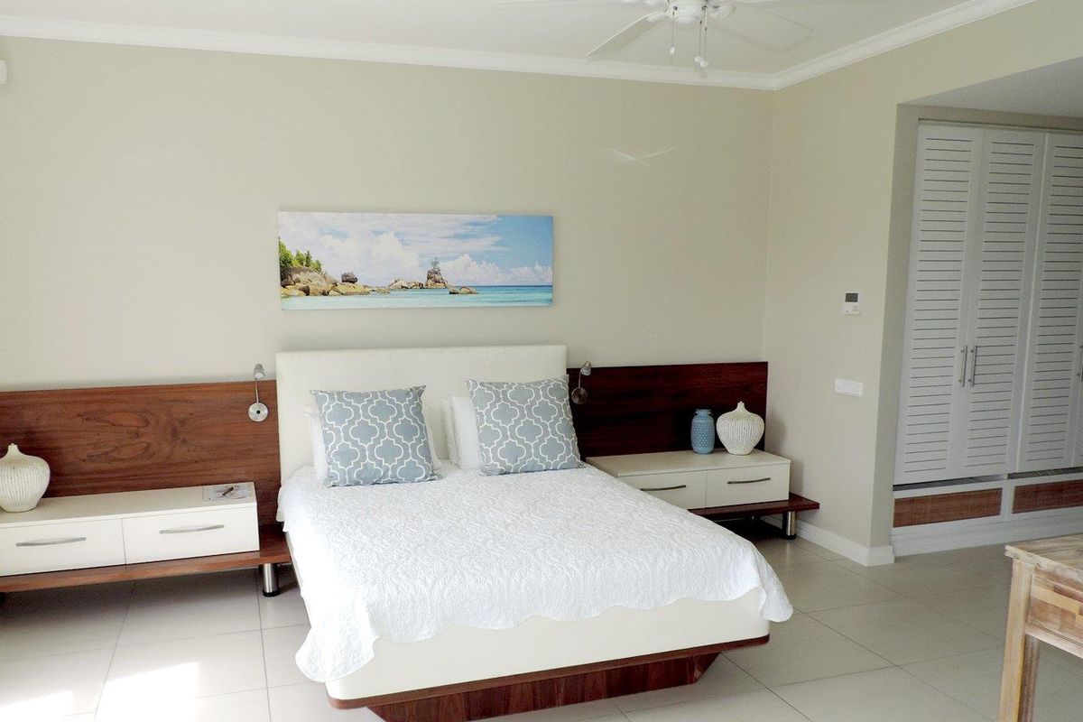 A well-maintained bedroom featuring built-in wooden headboard cabinetry, integrated bedside tables, a ceiling fan, and white louvered closet doors.