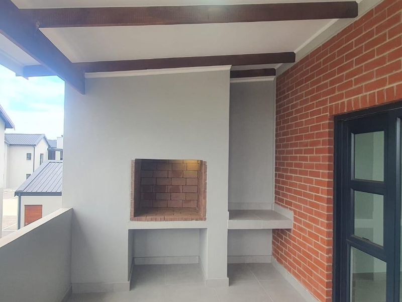 Covered balcony featuring a built-in braai, exposed timber beams, and a feature brick wall, providing a functional outdoor entertainment space.