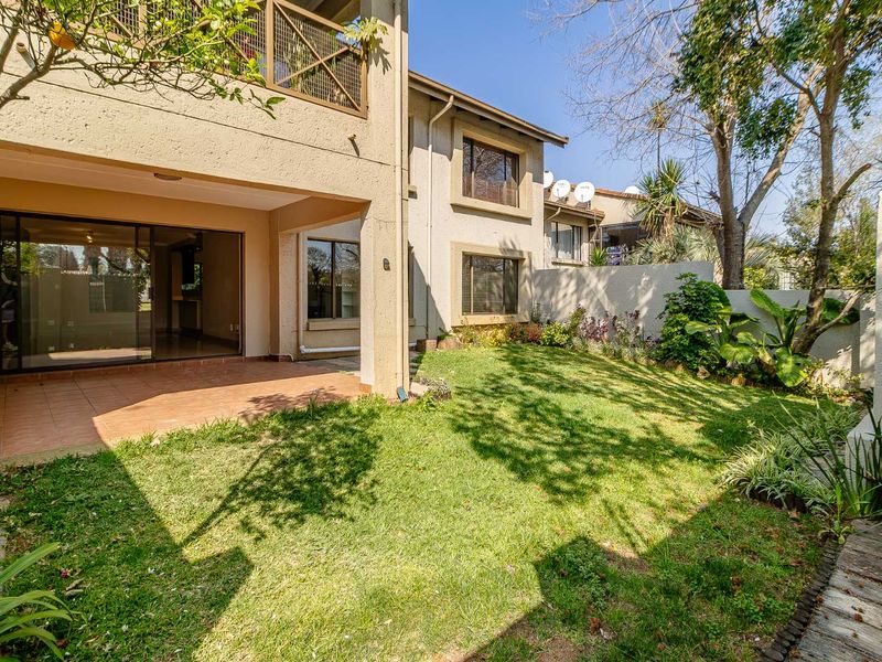 Rear view of the townhouse featuring a covered patio, sliding glass doors, a private garden, and an upper-level balcony with metal railings.