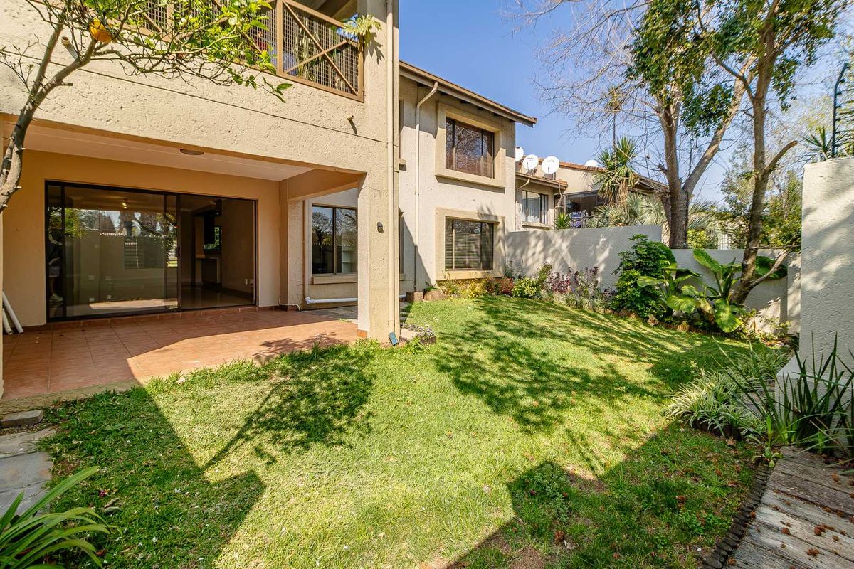 Rear view of the townhouse featuring a covered patio, sliding glass doors, a private garden, and an upper-level balcony with metal railings.