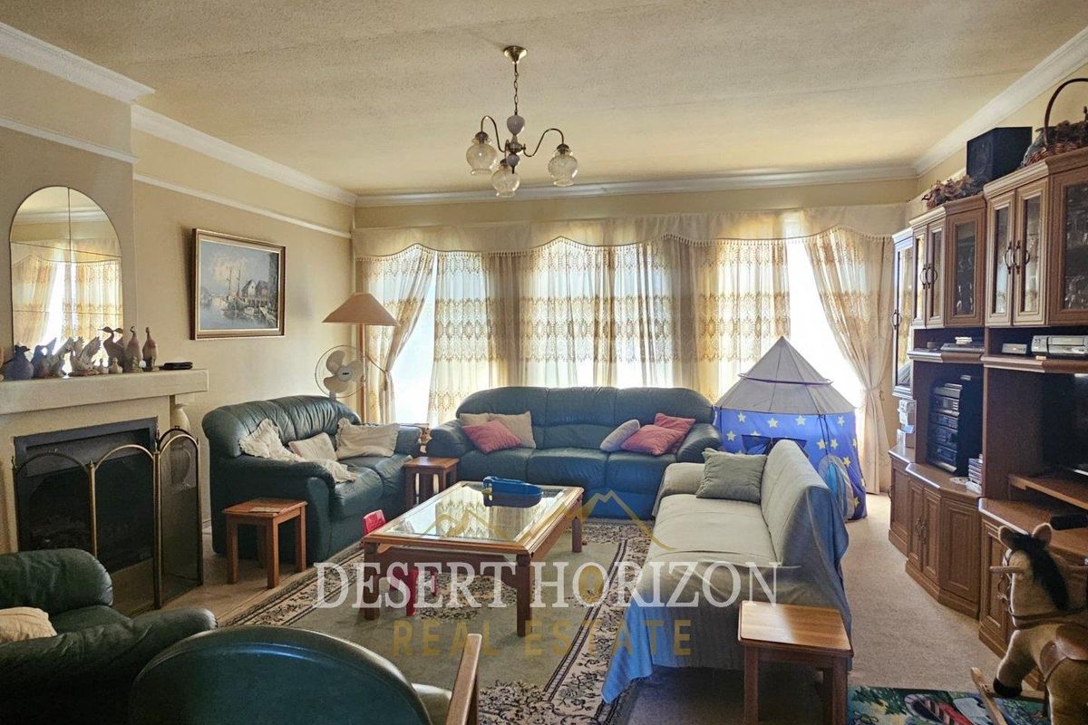 A spacious living room featuring a traditional fireplace, large window with curtains, and crown molding, offering a comfortable and classic living space.