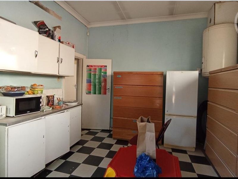 A dated kitchen area featuring original cabinetry, tiled flooring, and a wall-mounted electric water heater, requiring modernization and cosmetic updates.