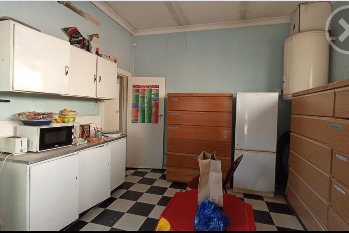 A dated kitchen area featuring original cabinetry, tiled flooring, and a wall-mounted electric water heater, requiring modernization and cosmetic updates.