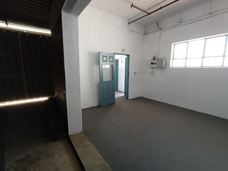 An empty industrial utility space featuring exposed ceiling pipes, a distribution board, and painted concrete flooring, suitable for storage or workshop use.