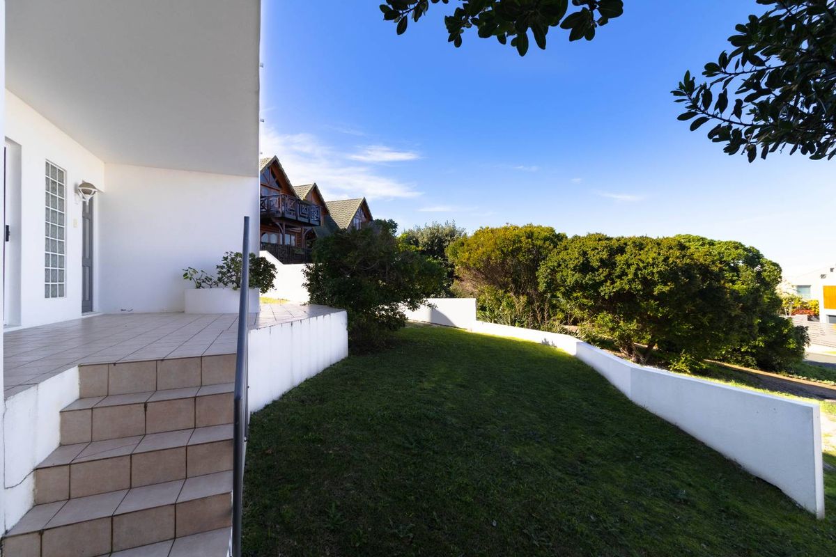 A view of the rear exterior featuring a tiled patio area, retaining walls, and a landscaped garden space.