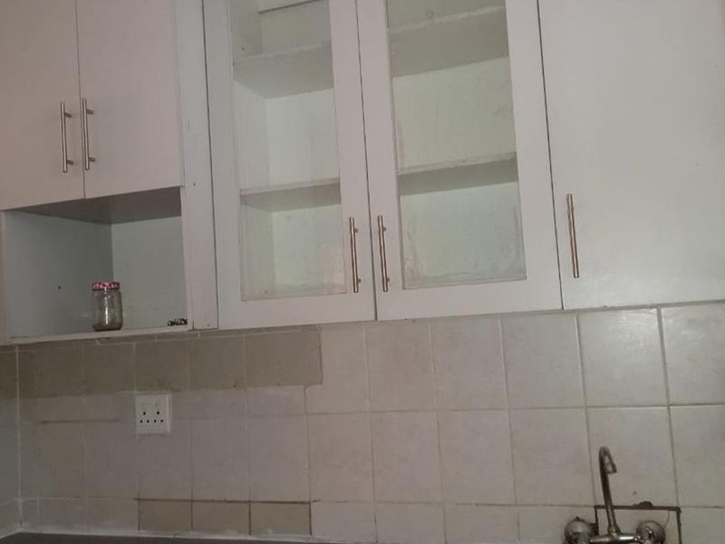A compact kitchen area featuring white built-in cabinetry, a stainless steel sink, and a tiled backsplash, currently in need of cosmetic updates.