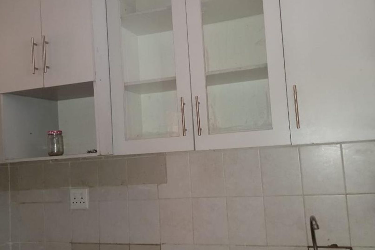 A compact kitchen area featuring white built-in cabinetry, a stainless steel sink, and a tiled backsplash, currently in need of cosmetic updates.