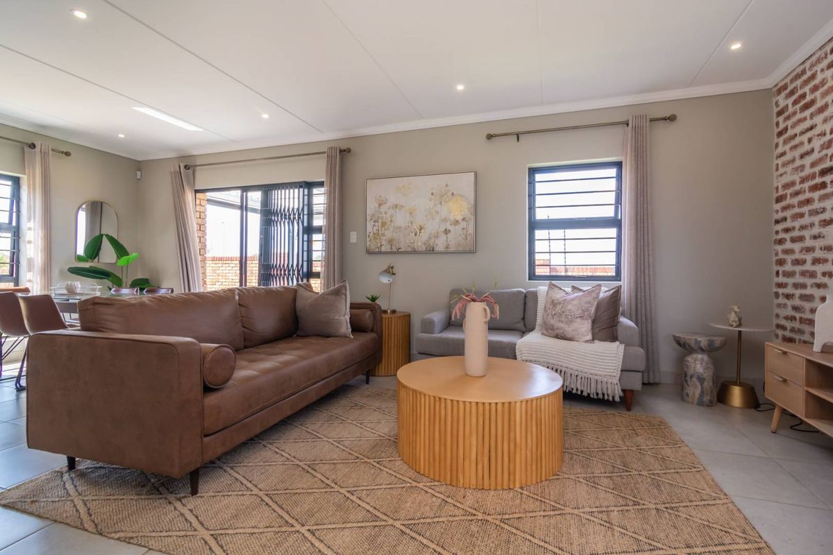 Spacious living room featuring an exposed brick accent wall, neutral tiled flooring, and recessed lighting, creating a warm and inviting atmosphere.