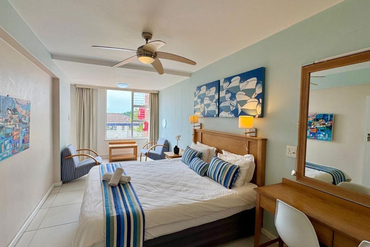 A well-lit bedroom featuring tiled flooring, a ceiling fan, and a large window providing natural light and exterior views.