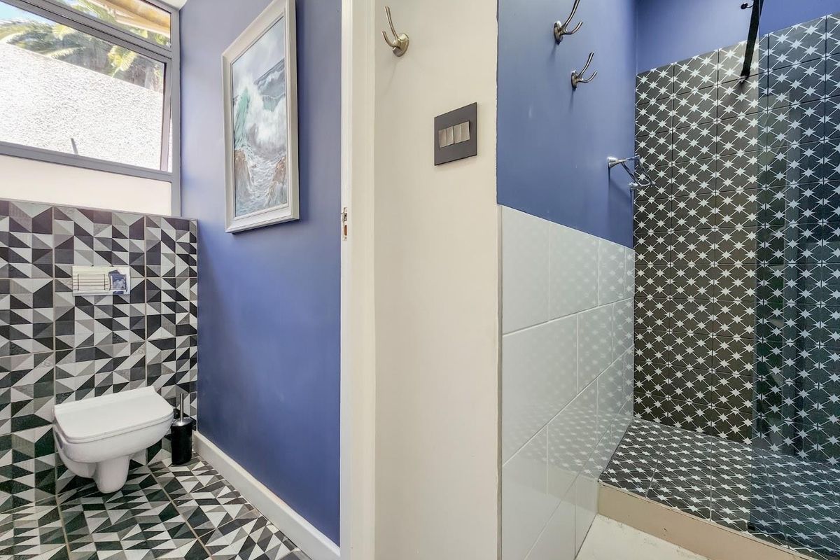 A modern bathroom featuring a wall-mounted toilet, a walk-in shower with patterned tiling, and blue accent walls.