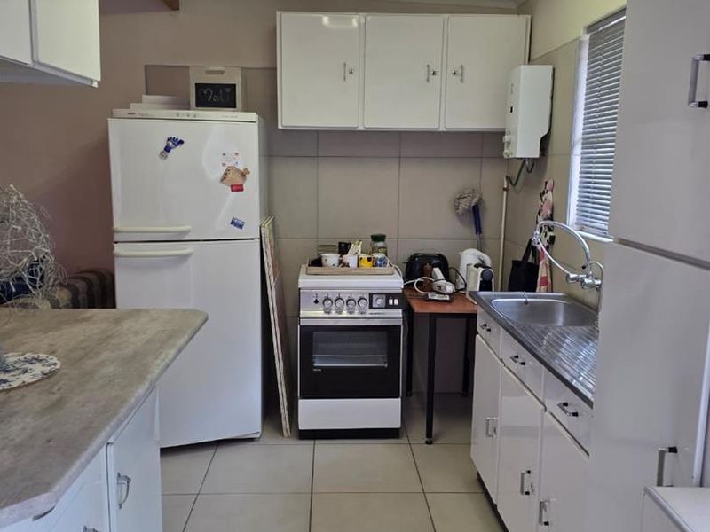 A functional kitchen featuring white cabinetry, tiled flooring, a stainless steel sink, and a freestanding stove, offering potential for modern updates.