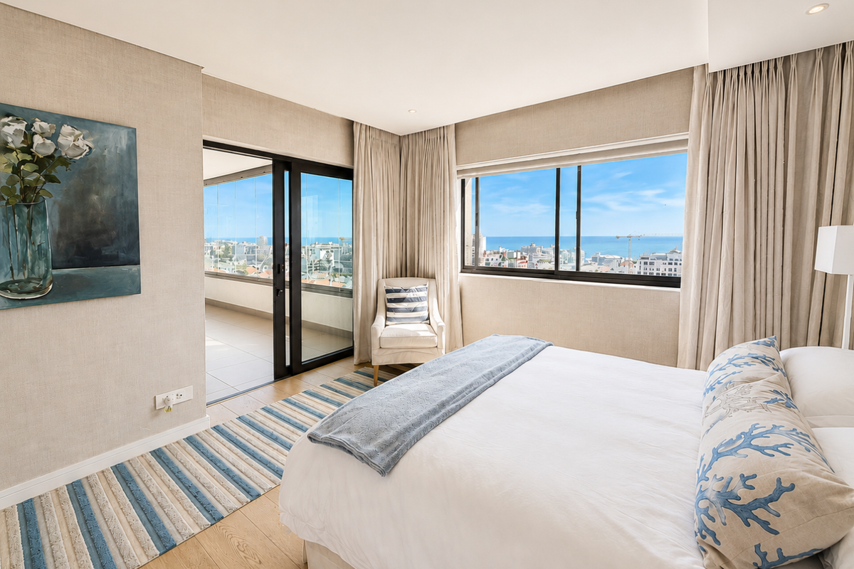 A bright, well-maintained bedroom featuring modern finishes, recessed lighting, and direct access to a balcony with expansive coastal and city views.