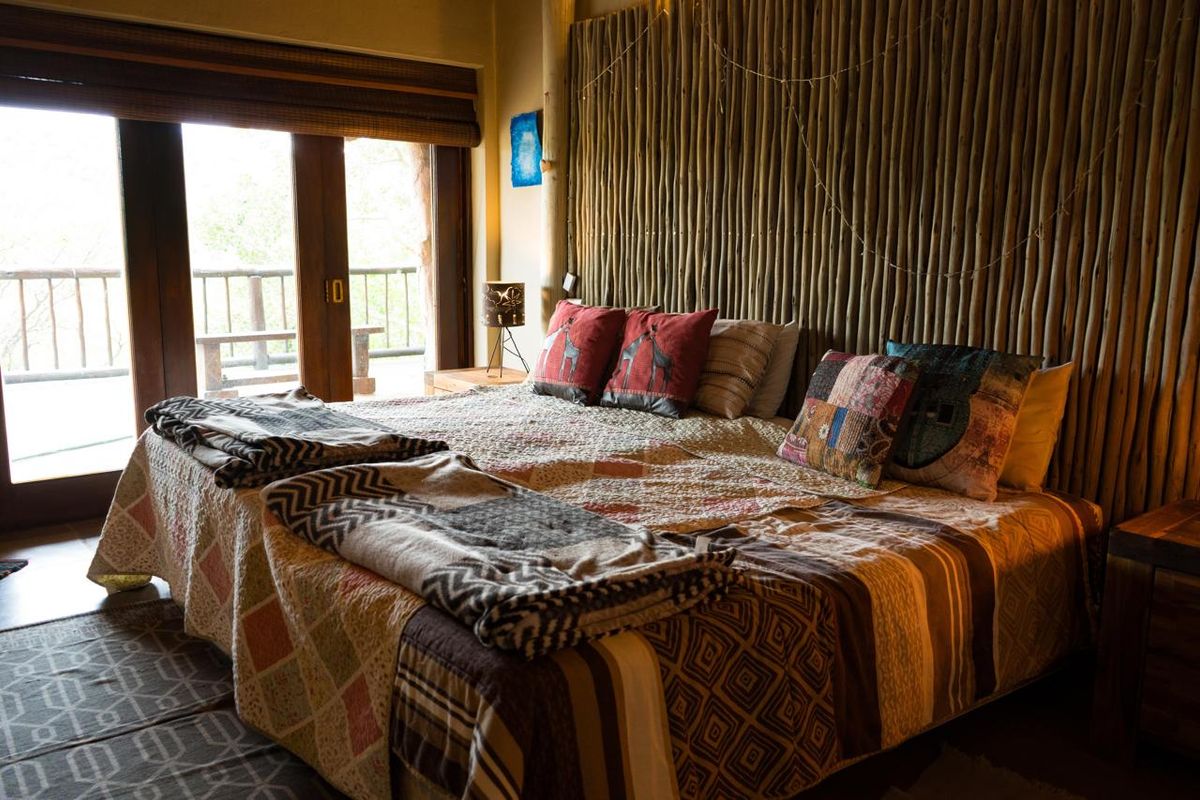 A rustic bedroom featuring unique timber pole wall cladding and direct access to an outdoor deck through sliding glass doors.
