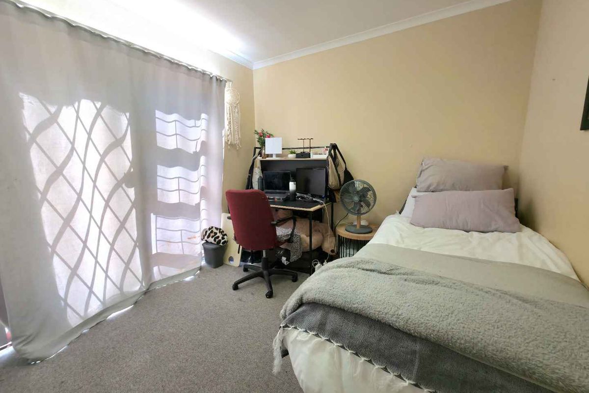 A functional bedroom featuring neutral wall tones, carpeted flooring, and a sliding glass door providing natural light.