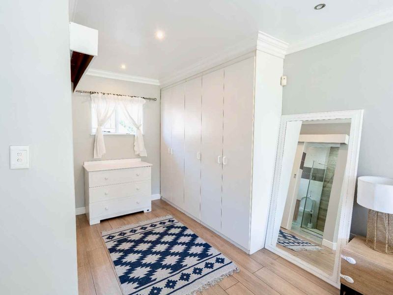 A bright bedroom featuring extensive built-in cupboards, modern laminate flooring, and crisp white finishes, offering ample storage and a clean, contemporary aesthetic.