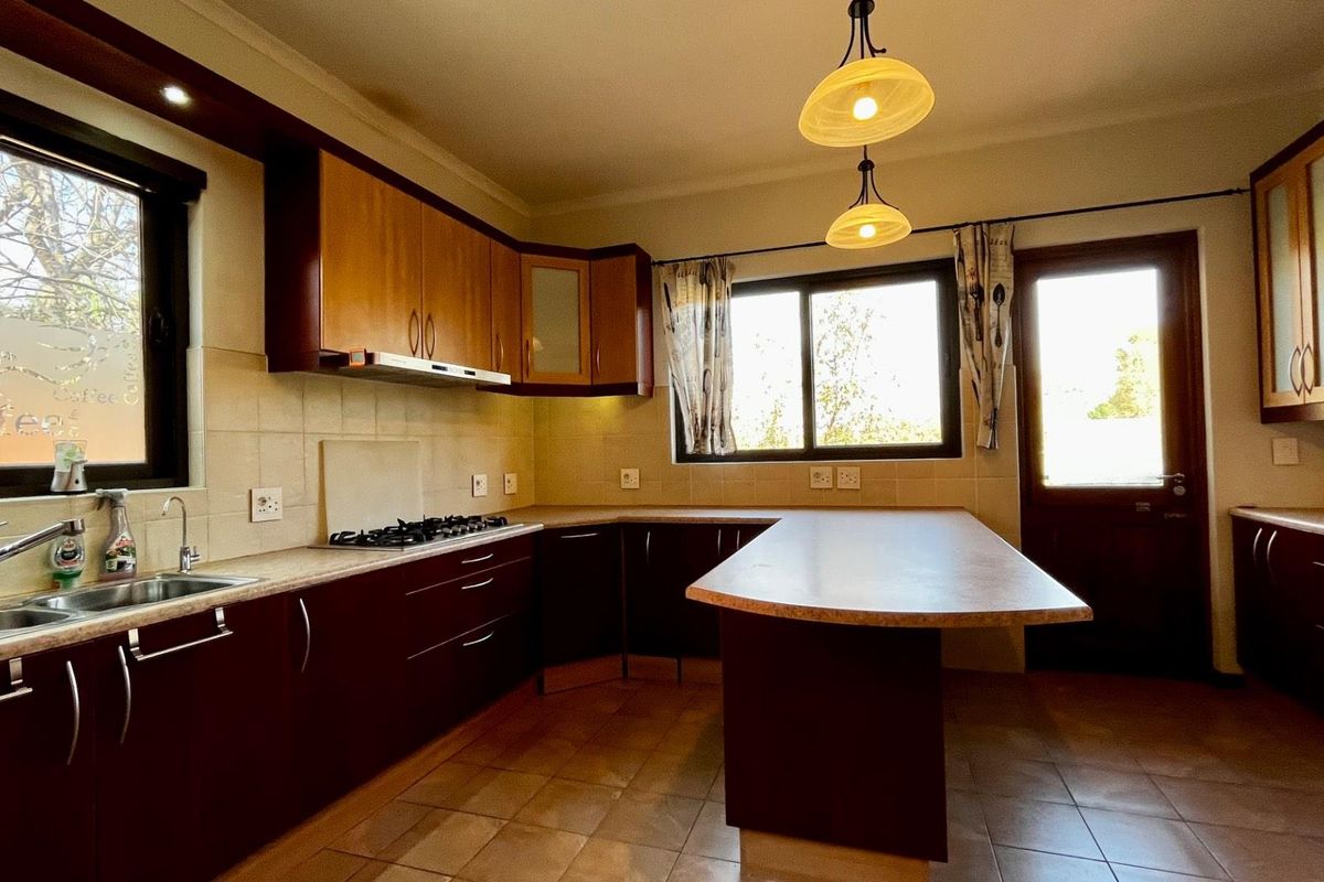 A functional kitchen featuring dark wood cabinetry, laminate countertops, a gas hob with extractor, and tiled flooring with direct outdoor access.