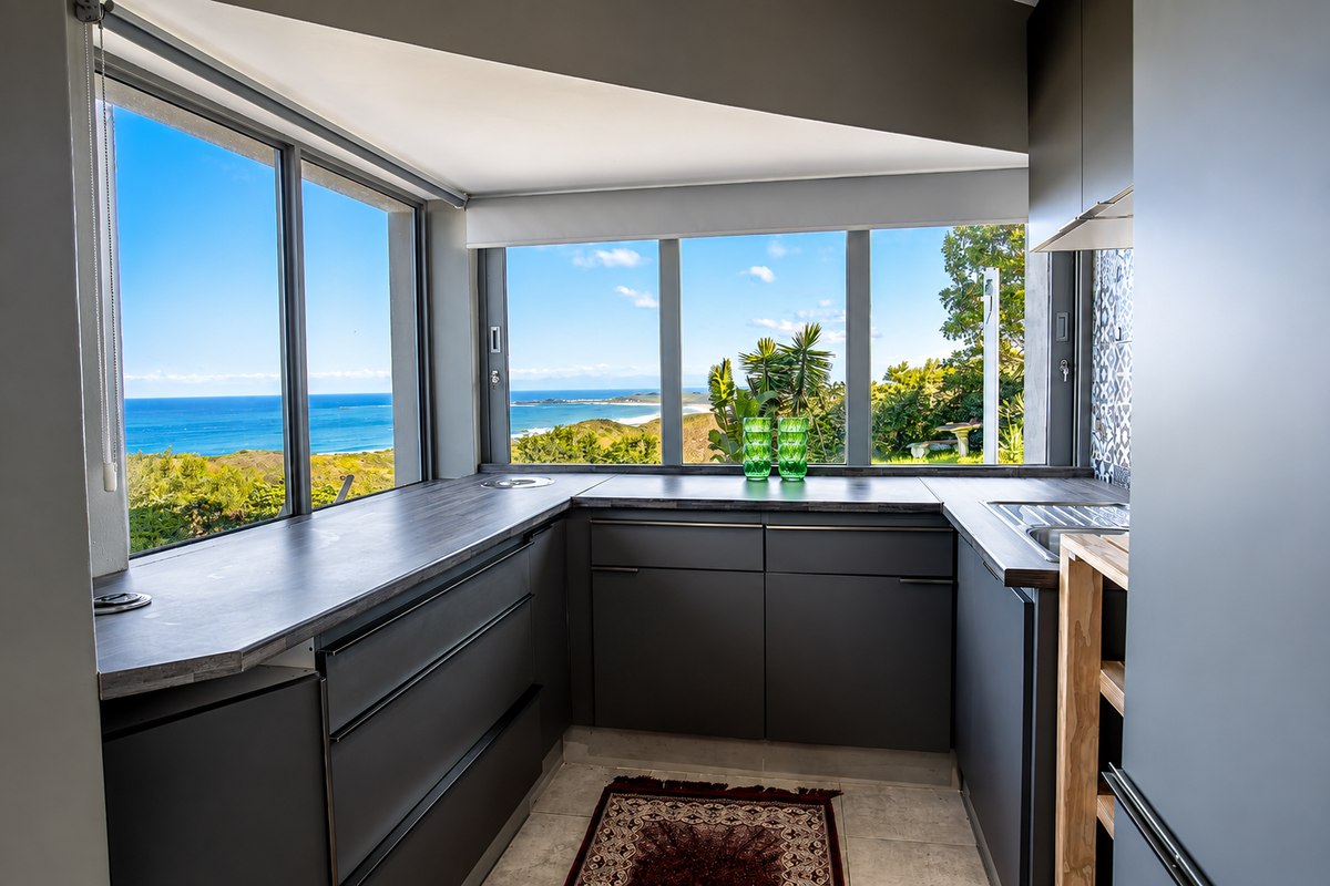 Modern kitchen featuring dark grey cabinetry, laminate countertops, and expansive windows offering panoramic ocean views.
