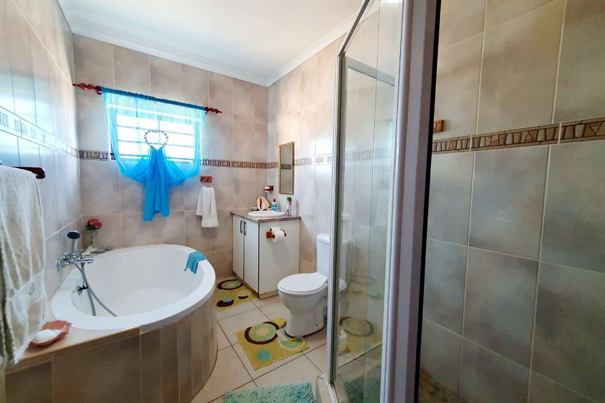 A functional bathroom featuring a corner soaking tub, a separate glass-enclosed shower, a vanity cabinet, and a toilet, finished with neutral wall and floor tiles.