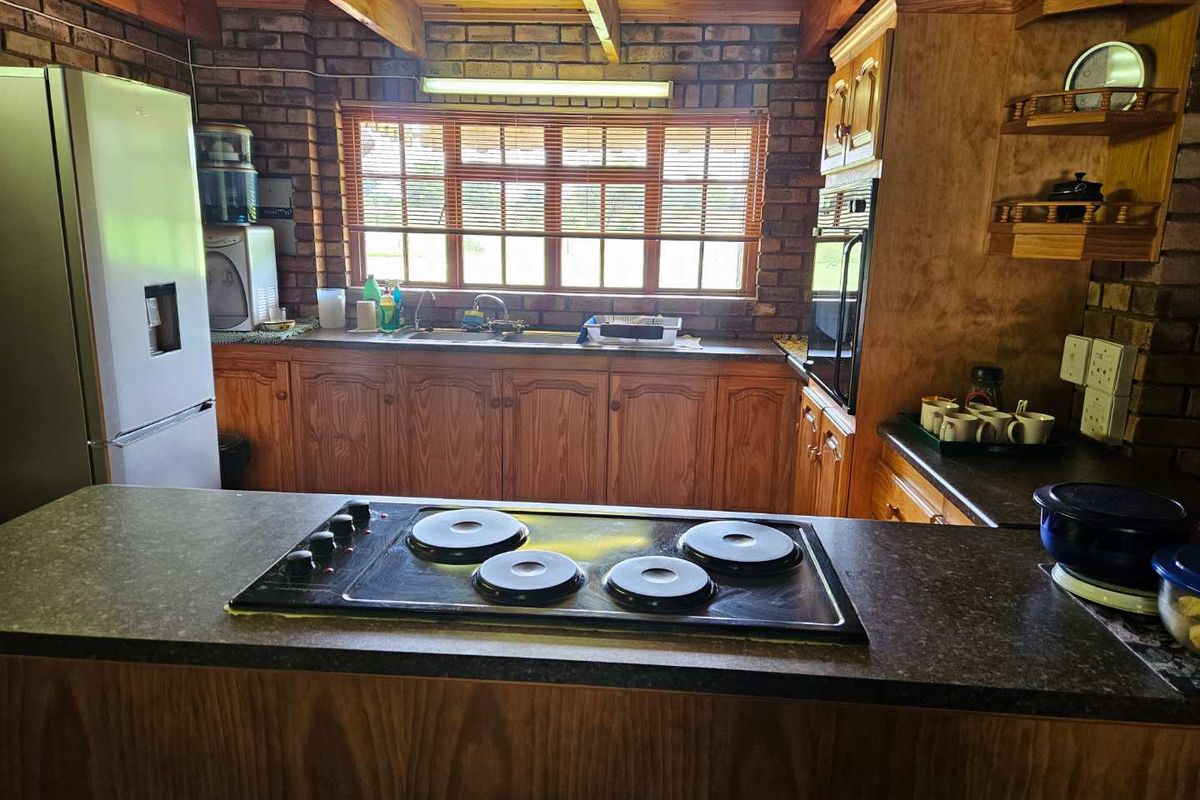 A rustic kitchen featuring exposed brick walls, timber ceiling beams, wooden cabinetry, and a built-in hob on the breakfast counter.