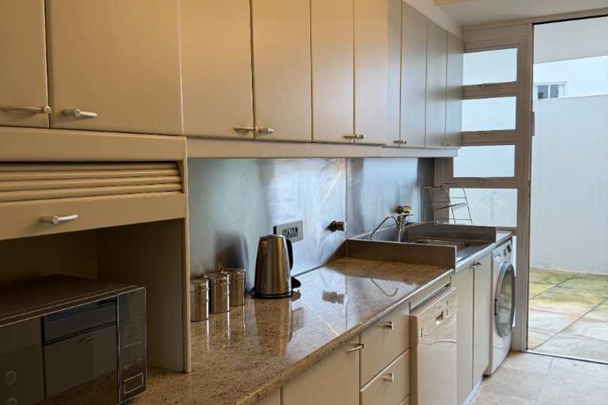A functional kitchen featuring granite countertops, stainless steel backsplash, ample built-in cabinetry, and direct access to an outdoor patio area.