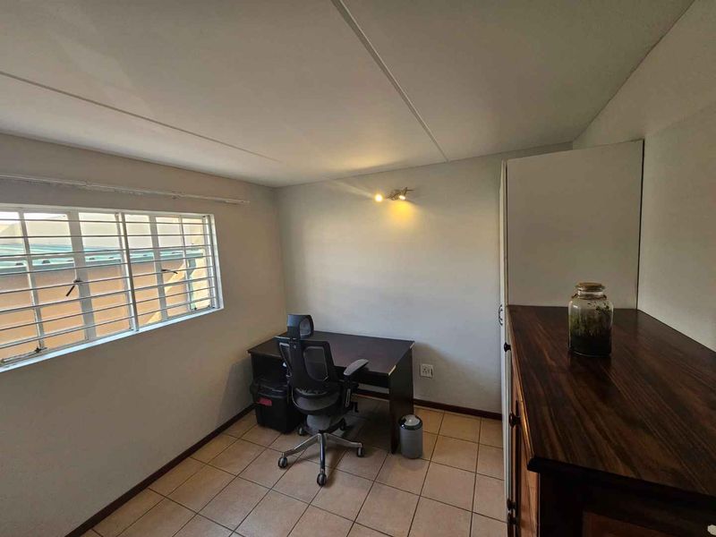 A functional bedroom featuring tiled flooring, a built-in cupboard, and security bars on the window, providing a practical space for rest or work.