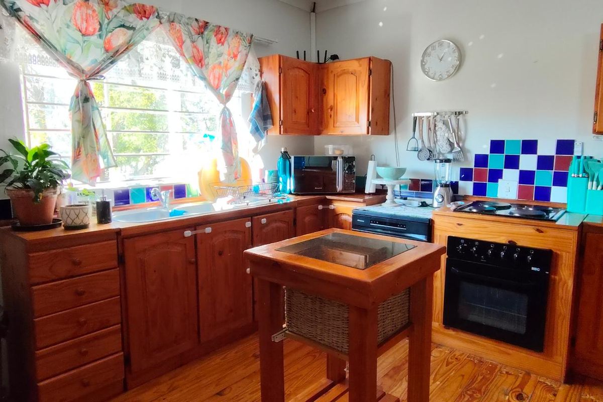 A functional kitchen featuring traditional wooden cabinetry, a built-in oven with hob, tiled splashback, and warm wooden flooring.