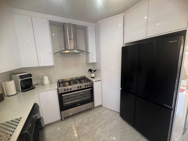 Modern kitchen featuring high-gloss white cabinetry, stone countertops, a stainless steel gas stove with extractor fan, and large format floor tiles.