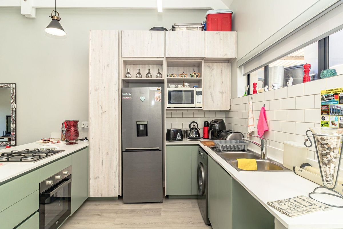 Modern kitchen featuring light wood-grain cabinetry, sage green base units, white subway tile backsplash, integrated oven, gas hob, and stainless steel double sink.