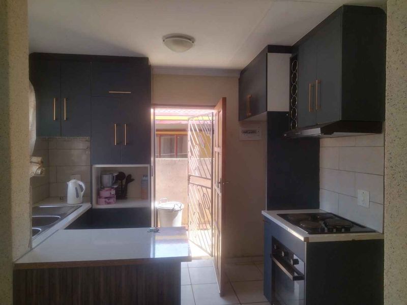 A functional kitchen featuring dark cabinetry, a built-in oven and hob, extractor fan, and a double sink with direct access to the exterior.
